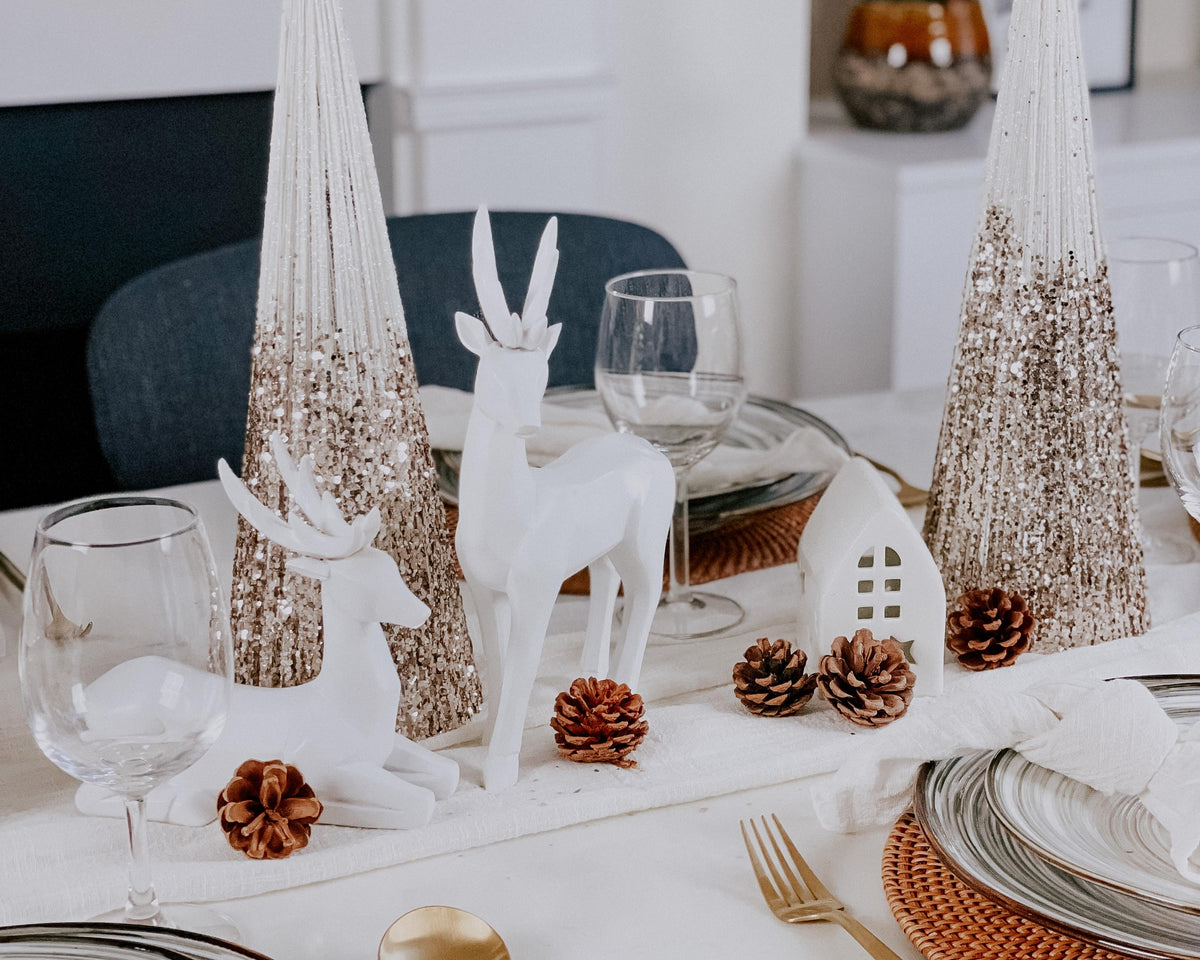 Gold glitter cone trees on a Christmas table with white reindeer and pine cones