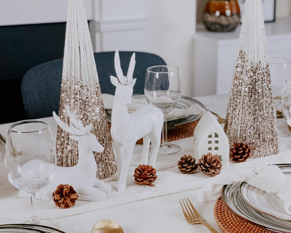 Gold glitter cone trees on a Christmas table with white reindeer and pine cones