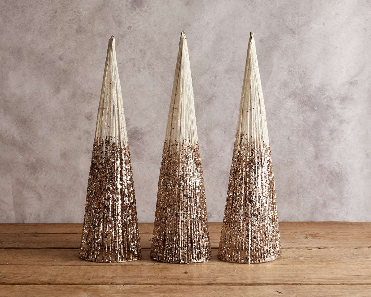 Three cream and gold glitter Christmas cone trees on a wooden table