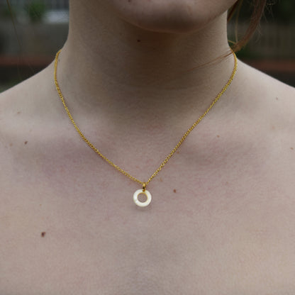 Close-up of the mother of pearl circle pendant necklace worn at the collarbone
