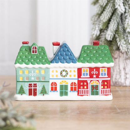 Ceramic Christmas street of green, blue and red houses on a wooden table beside a snowy tree