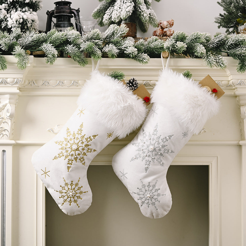 Two white plush snowflake Christmas stockings with faux fur cuffs hanging on a fireplace