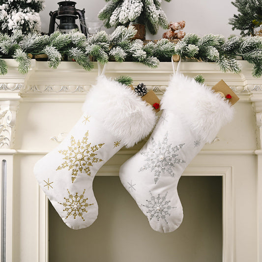 Two white plush snowflake Christmas stockings with faux fur cuffs hanging on a fireplace