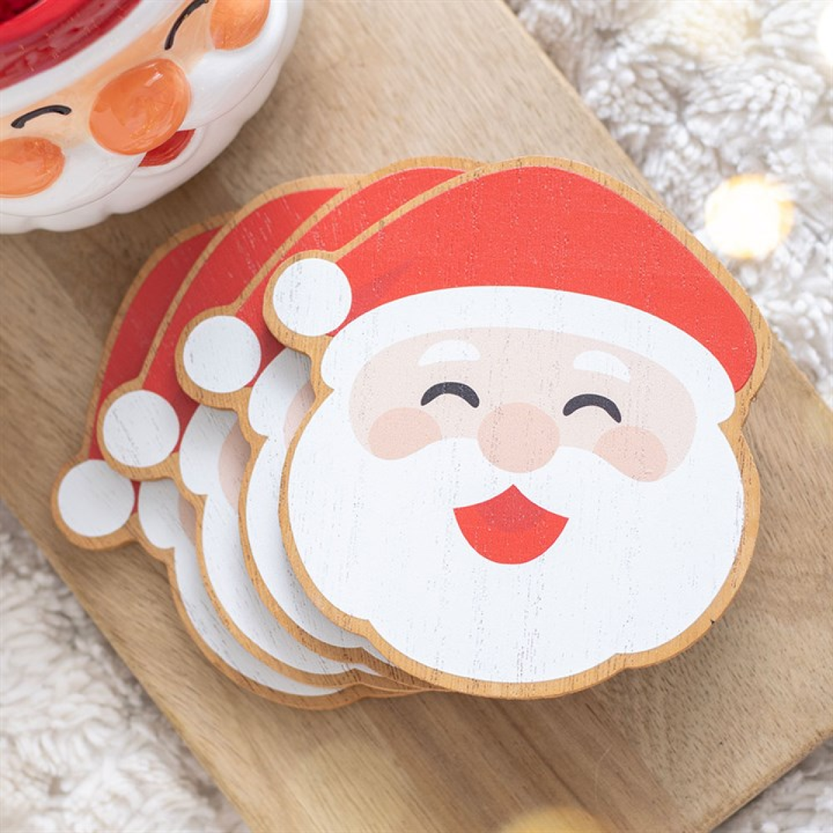 Stack of four smiling Santa face Christmas coasters on a wooden board