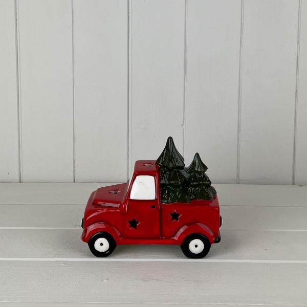 Red ceramic Christmas truck carrying fir trees on a white wooden shelf