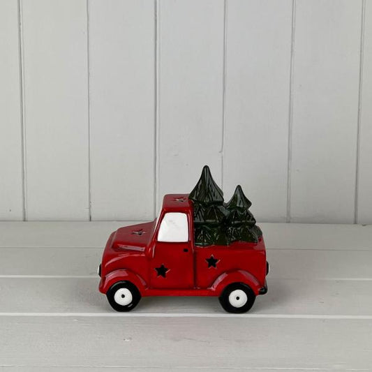 Red ceramic Christmas truck carrying fir trees on a white wooden shelf