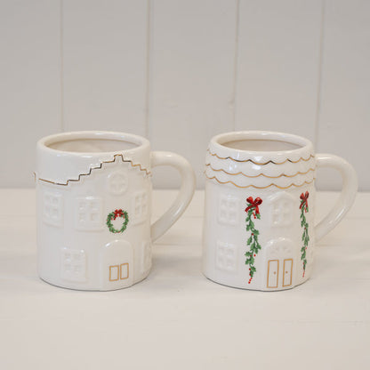 Two Christmas house mugs side by side; the holly garland design is on the right